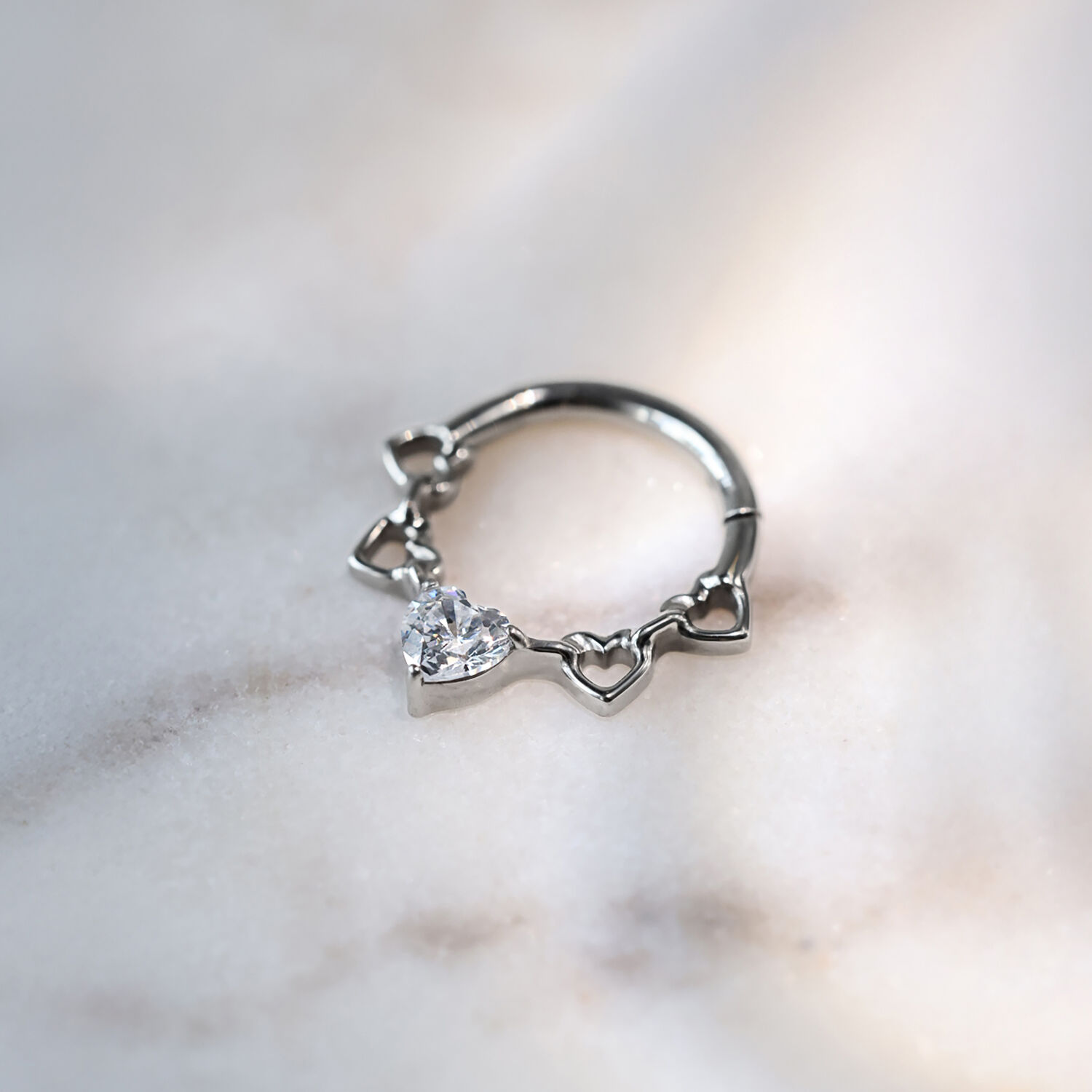 Clicker de septum en titane argenté avec design de cœur et cristaux sur fond marbré