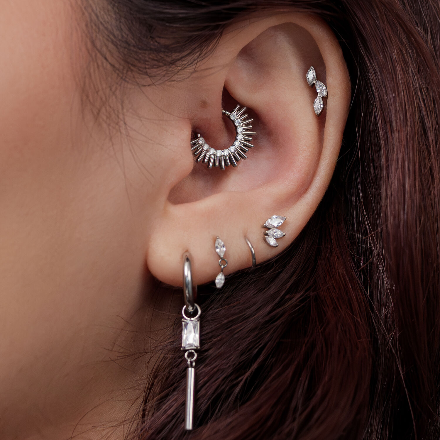 Gros plan d'une oreille avec plusieurs boucles d'oreilles argentées, dont une bague pointue et remarquable dans la zone interne de l'oreille.