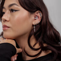 Boucles d'oreilles argentées avec design de lune et de boule Femme avec plusieurs boucles d'oreilles argentées, motif lune et boules à l'oreille sur fond gris
