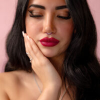 Femme aux cheveux noirs avec un piercing nasal argenté avec cristal rouge sur fond rose