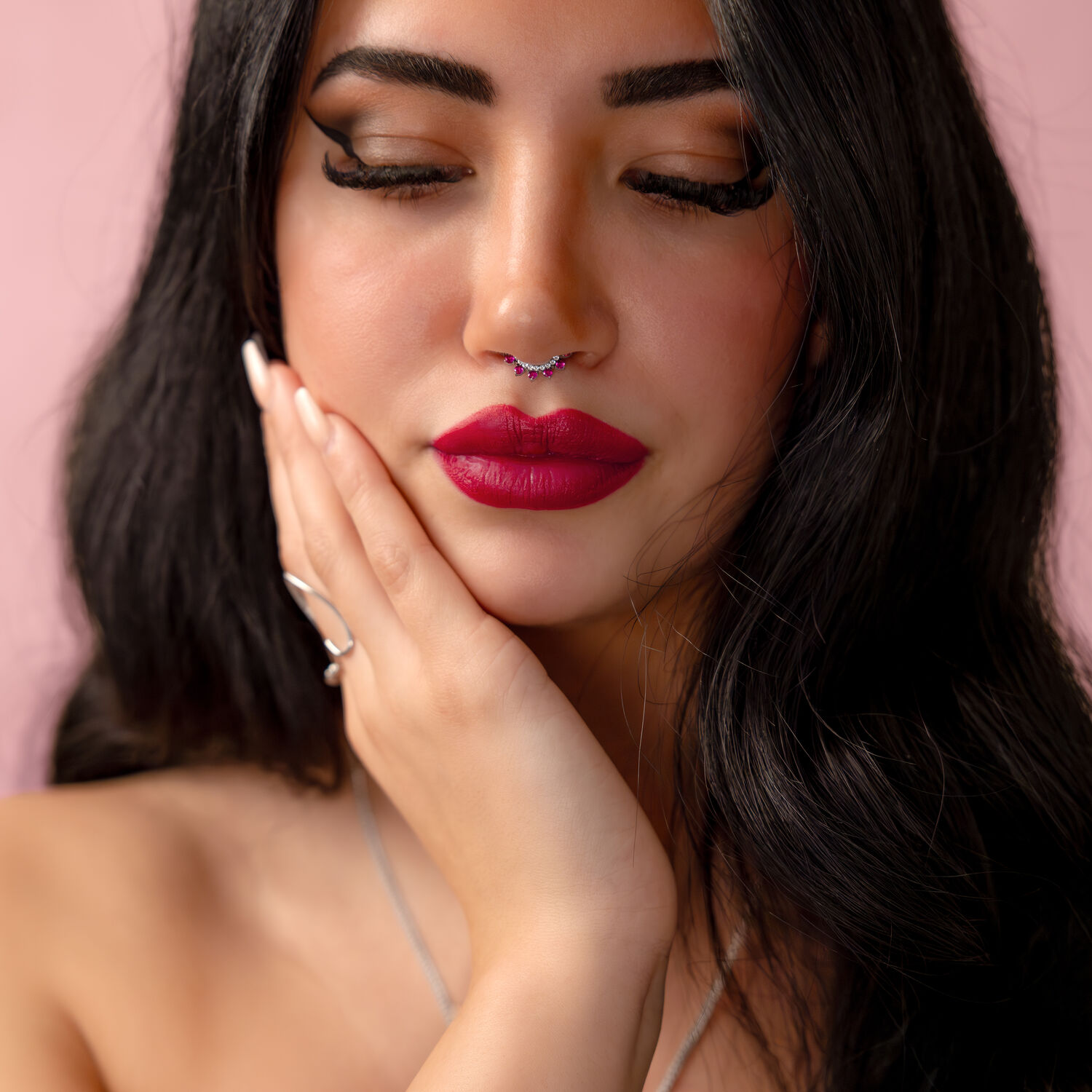 Femme aux cheveux noirs avec un piercing nasal argenté avec cristal rouge sur fond rose