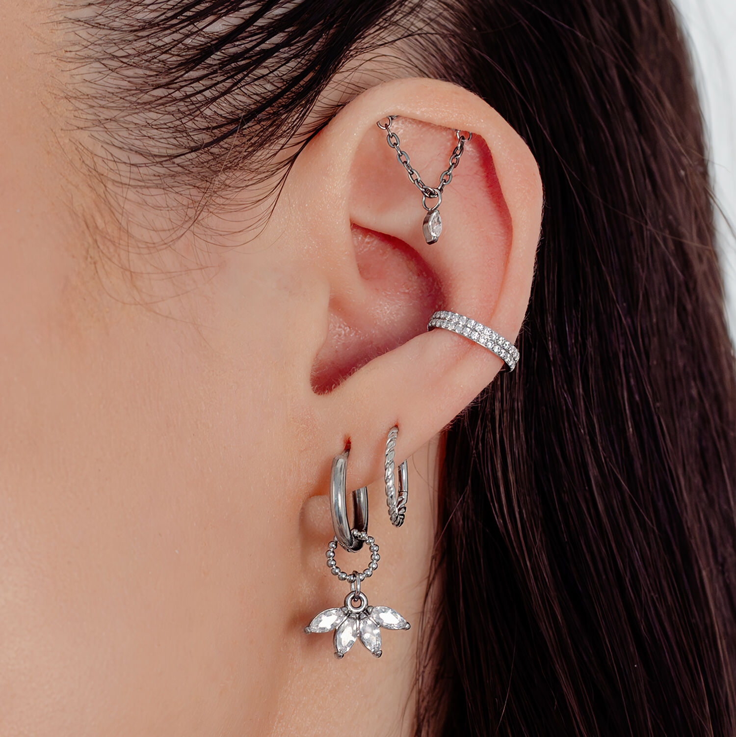 Boucles d'oreilles en cristal argenté avec pendentif éventail Gros plan d'une oreille avec plusieurs boucles d'oreilles argentées, dont un pendentif éventail avec des cristaux.