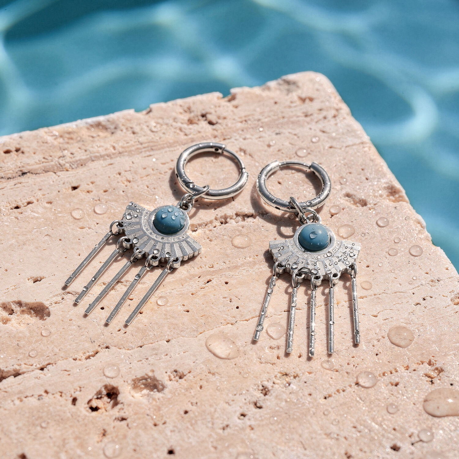 Boucles d'oreilles argentées avec détails en turquoise sur pierre mouillée au bord de la piscine