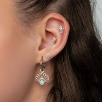 Ensemble de boucles d'oreilles en titane avec fleurs de jasmin Gros plan d'une oreille avec plusieurs boucles d'oreilles et piercings en forme de fleurs de jasmin en titane, sur fond blanc