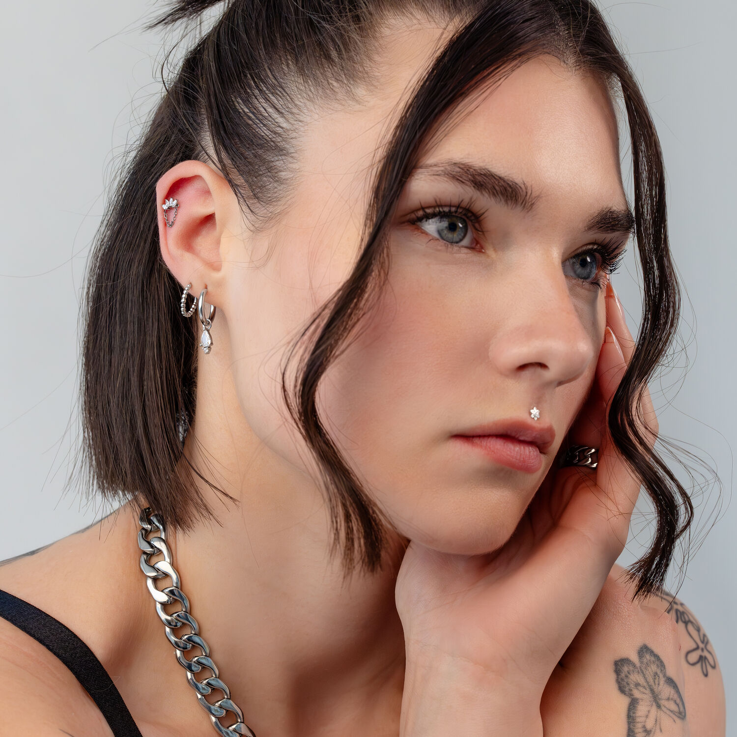 Piercings d'oreille en argent avec cristaux Gros plan d'un visage avec plusieurs piercings d'oreille en argent et détails en cristal sur fond gris