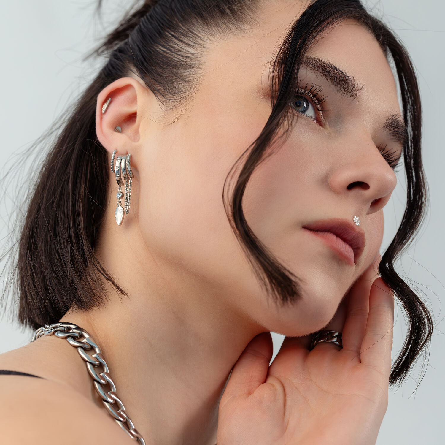 Boucles d'oreilles argentées avec chaîne et embout Gros plan d'une femme aux cheveux foncés portant des boucles d'oreilles argentées avec chaînes et un embout demi-ovale.