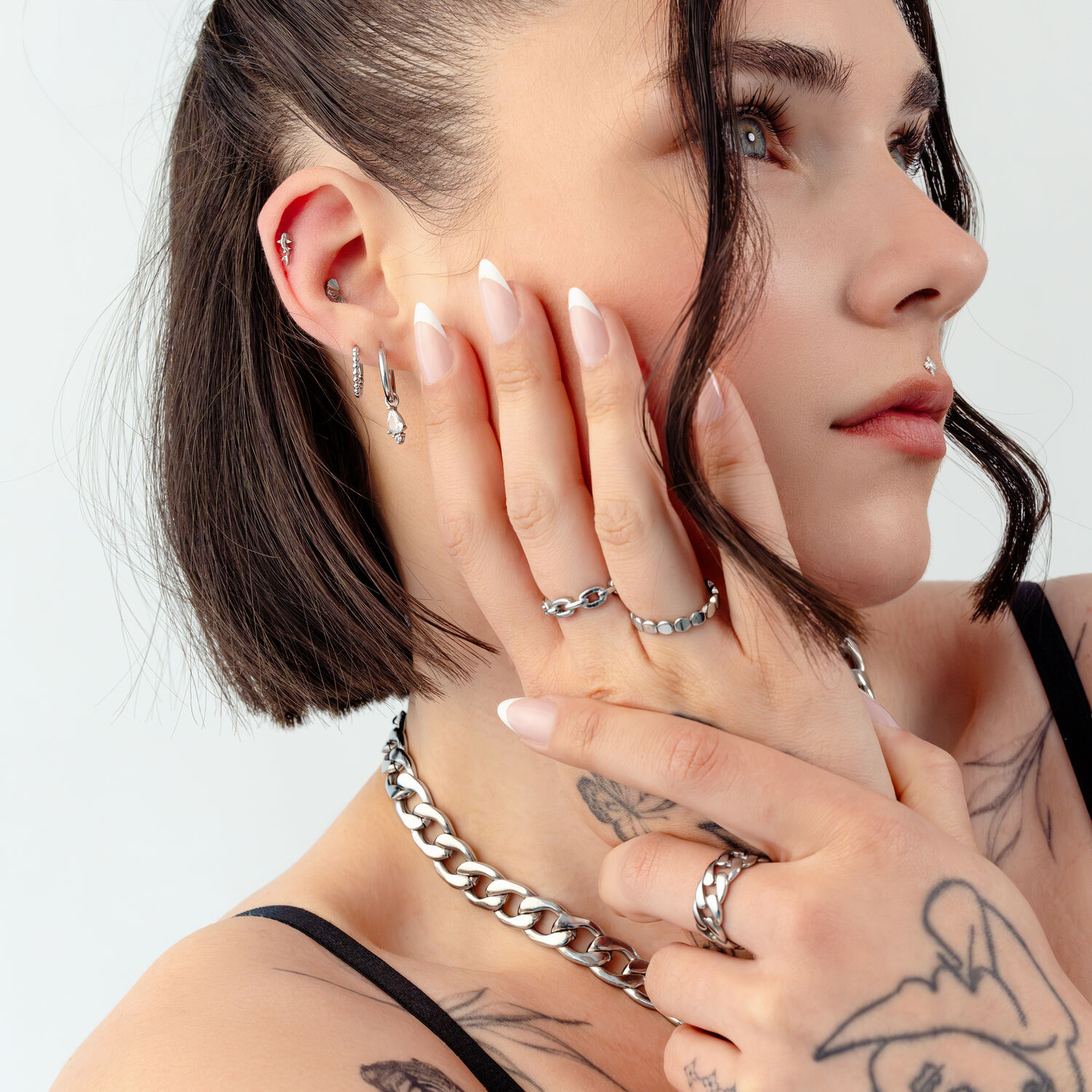 Bijoux en argent sur femme avec tatouages Femme aux cheveux courts, tatouages et divers bijoux en argent sur fond blanc