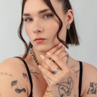 Femme aux cheveux courts portant une chaîne argentée et des boucles d'oreilles, tatouages visibles