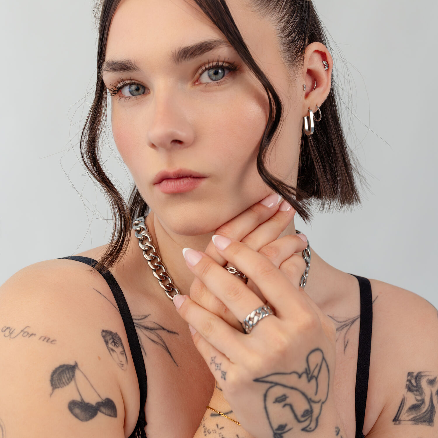 Femme aux cheveux courts portant une chaîne argentée et des boucles d'oreilles, tatouages visibles