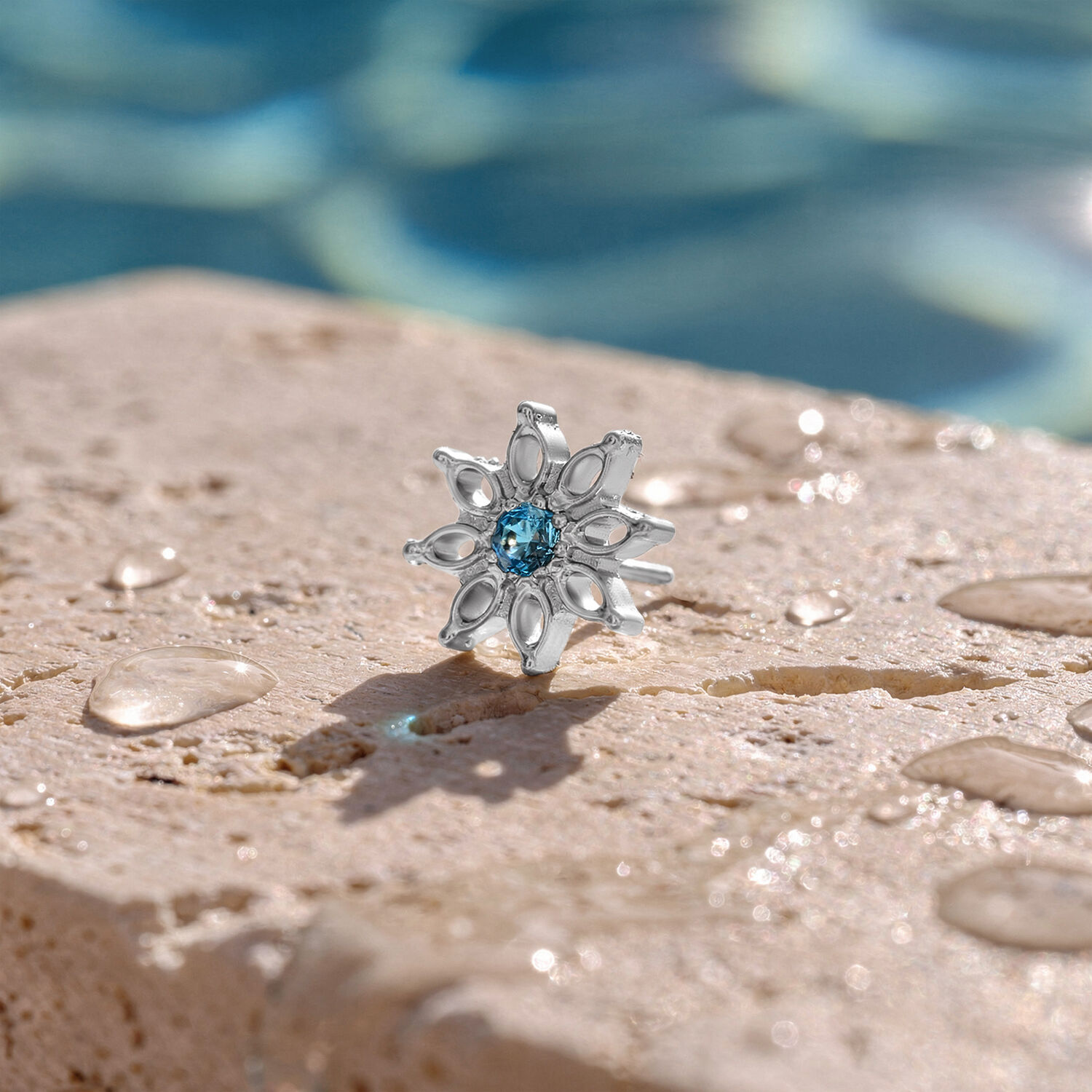 Embout Aqua Bloom en cristal turquoise Embout argenté avec cristal turquoise sur surface en pierre mouillée devant un arrière-plan flou de piscine