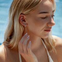 Boucle d'oreille en or blanc avec cristal turquoise Femme avec plusieurs boucles d'oreilles, dont une en or blanc avec cristal turquoise, sur fond bleu
