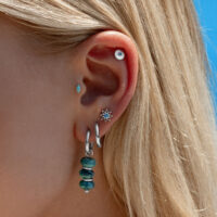 Embout d'oreille en cristal turquoise Oreille avec plusieurs piercings, y compris embout en cristal turquoise et créoles argentées, devant un ciel bleu