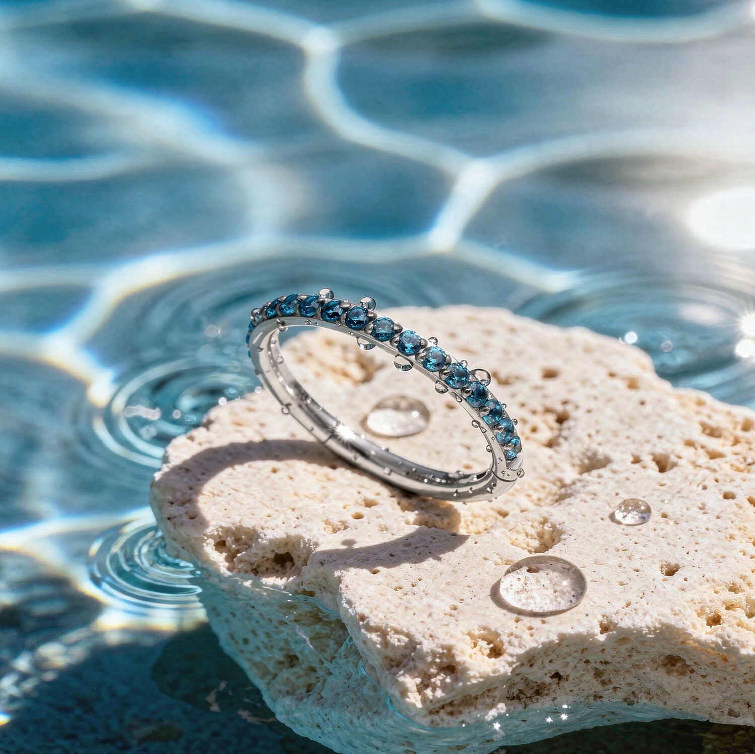 Bague en cristal turquoise sur pierre Bague en cristal turquoise sur une pierre claire au bord d'une piscine avec des reflets de soleil