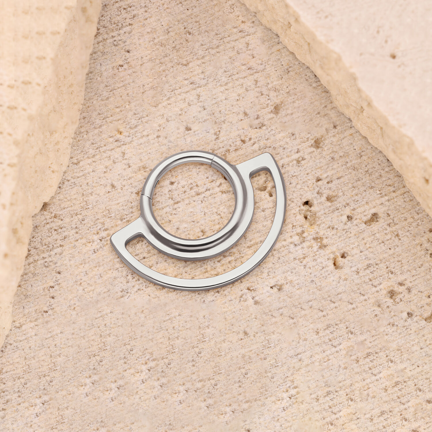 Clicker anneau en argent sur fond de pierre beige, design circulaire