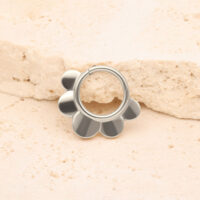 Clicker Half Flower argent en titane Clicker Half Flower argent devant une pierre beige sur fond clair