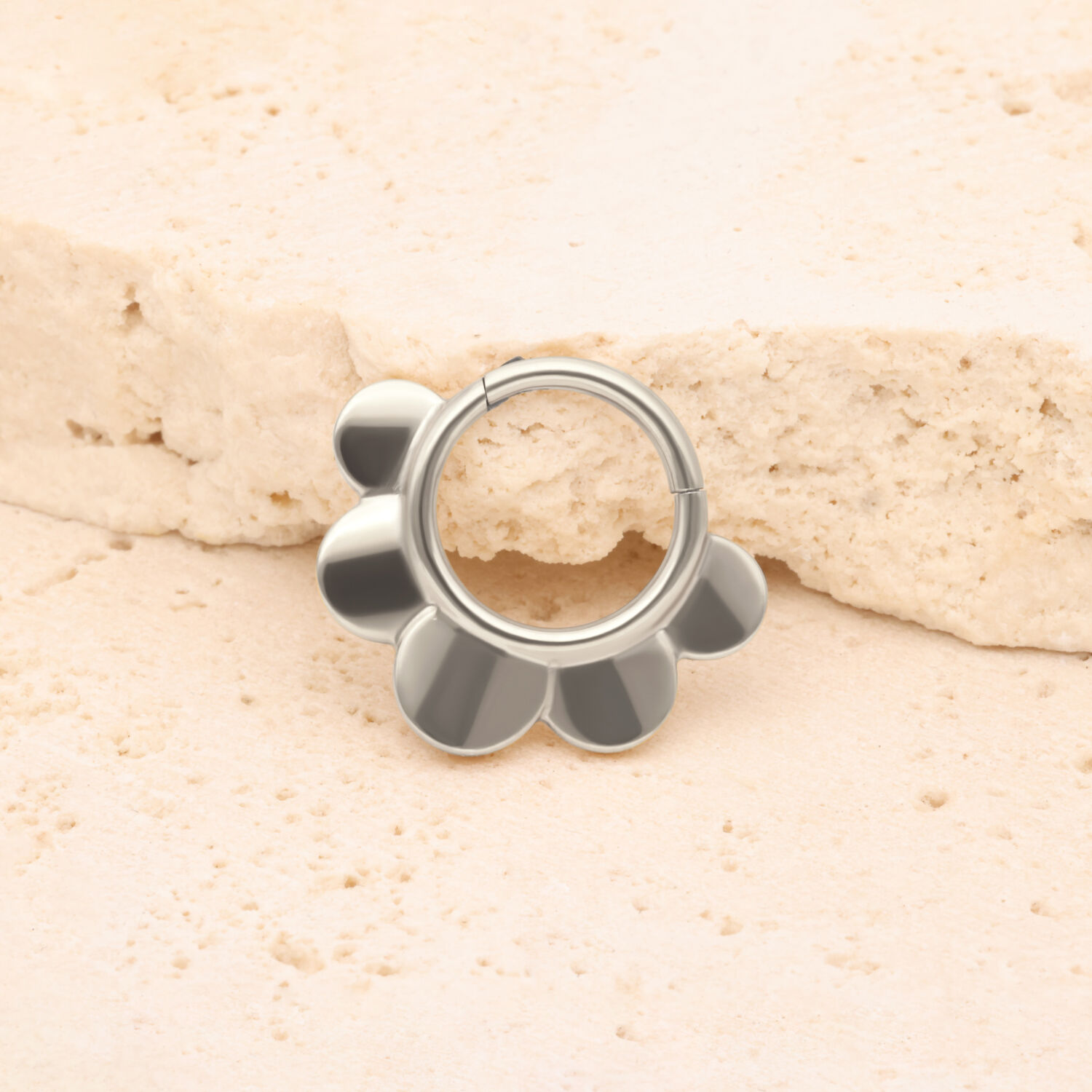 Clicker Half Flower argent en titane Clicker Half Flower argent devant une pierre beige sur fond clair