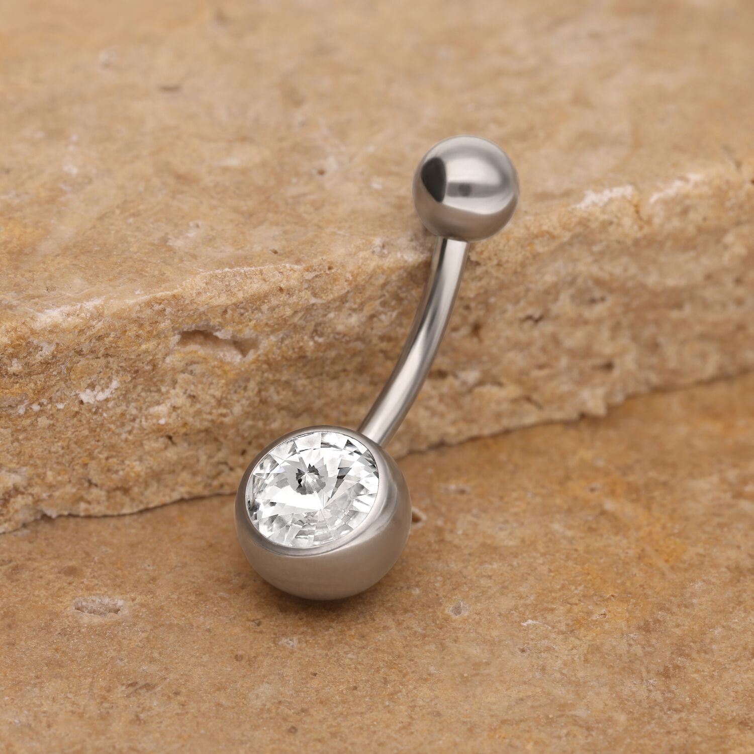 Banane de nombril en titane avec cristal Banane de nombril en argent avec cristal clair sur pierre beige